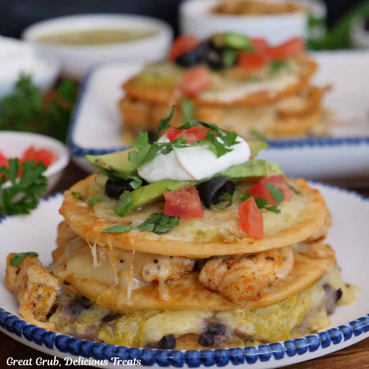 A white round plate with blue trim with a mini green chili chicken Mexican pizza on it with more in the background.