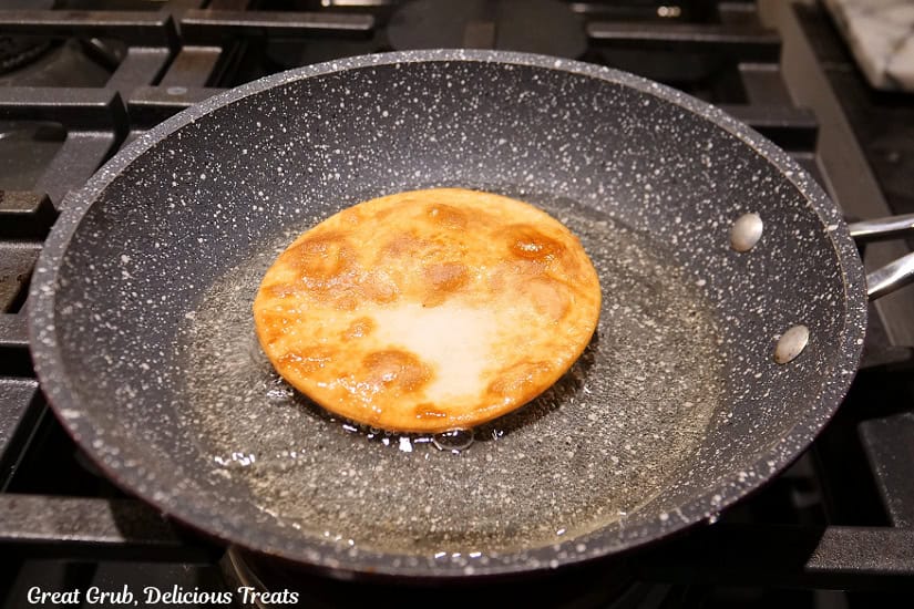A frying pan with a mini flour tortilla being fried in it.