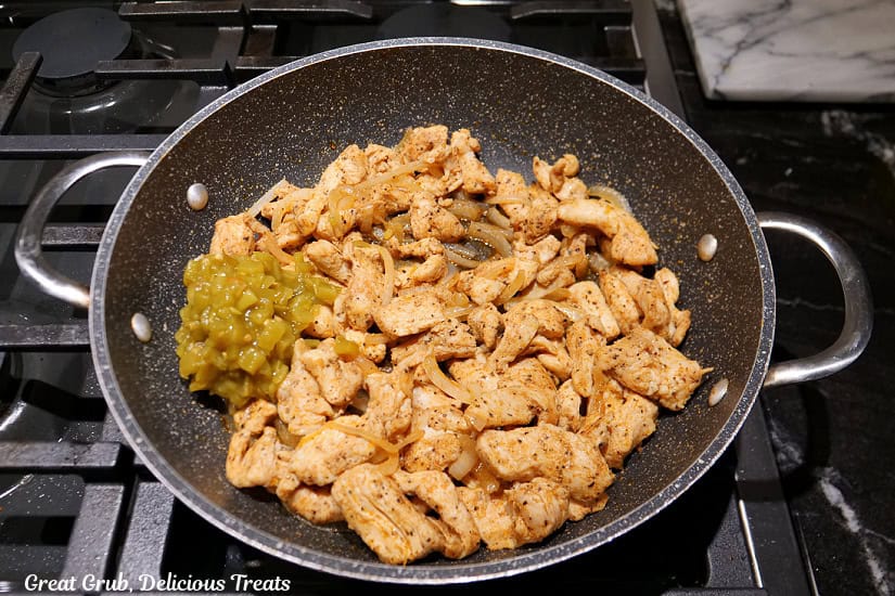 A frying pan with cooked chicken pieces and onions, and diced green chilies added to the pan.