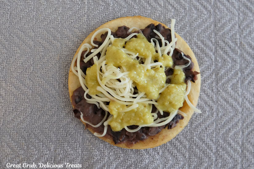 A mini flour tortilla with black beans, shredded jack cheese, and green sauce pour on it.