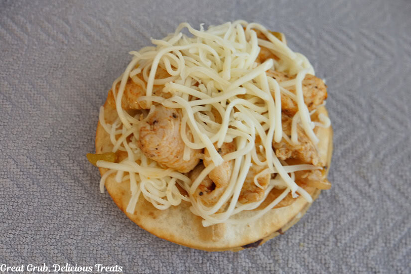 A mini flour tortilla with seasoned chicken pieces and shredded jack cheese on it.
