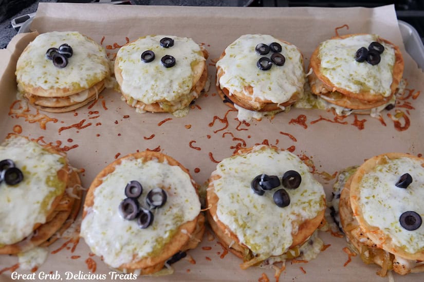 A baking sheet with eight mini green chili chicken Mexican pizzas on it after being pulled out of the oven.