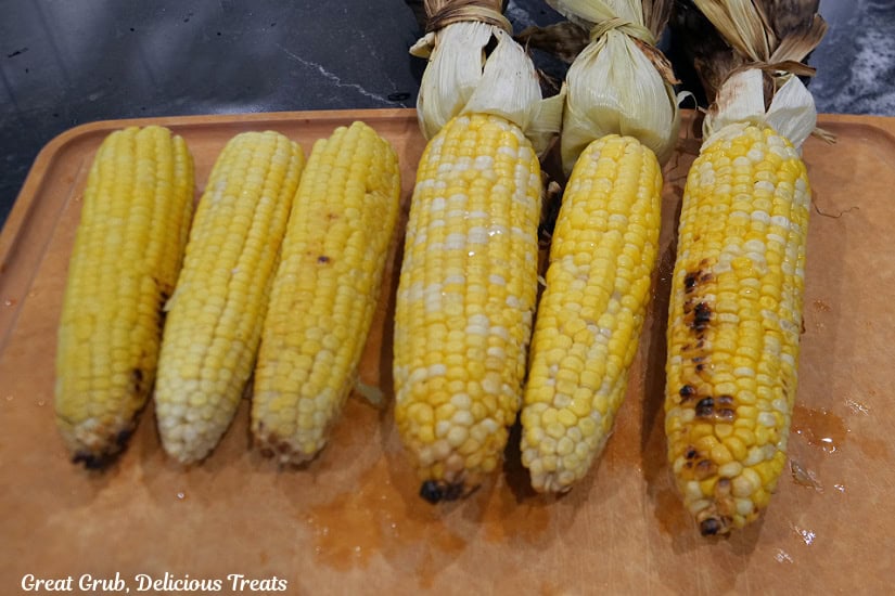 Six ears of corn on a wood cutting board with lime squeezed over them.
