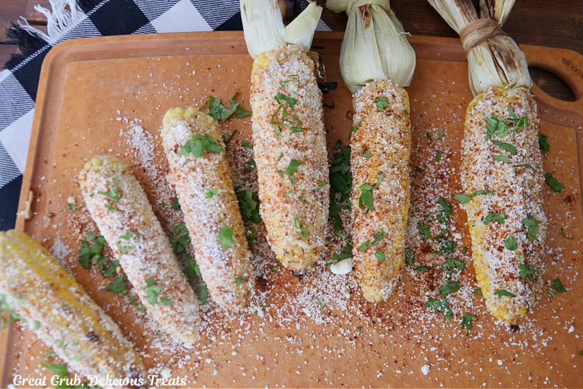 Six ears of corn with all the ingredients of Mexican street corn on them.