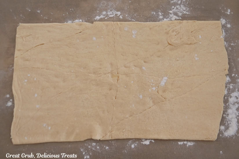 A counter top with crescent dough, on parchment paper, rolled into a rectangle.