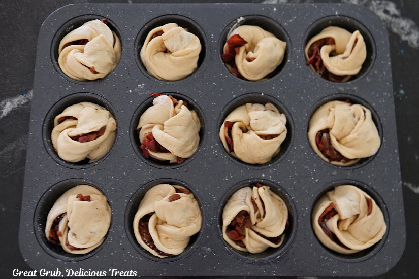 A muffin tin with twelve maple bacon muffins in it before it is baked.