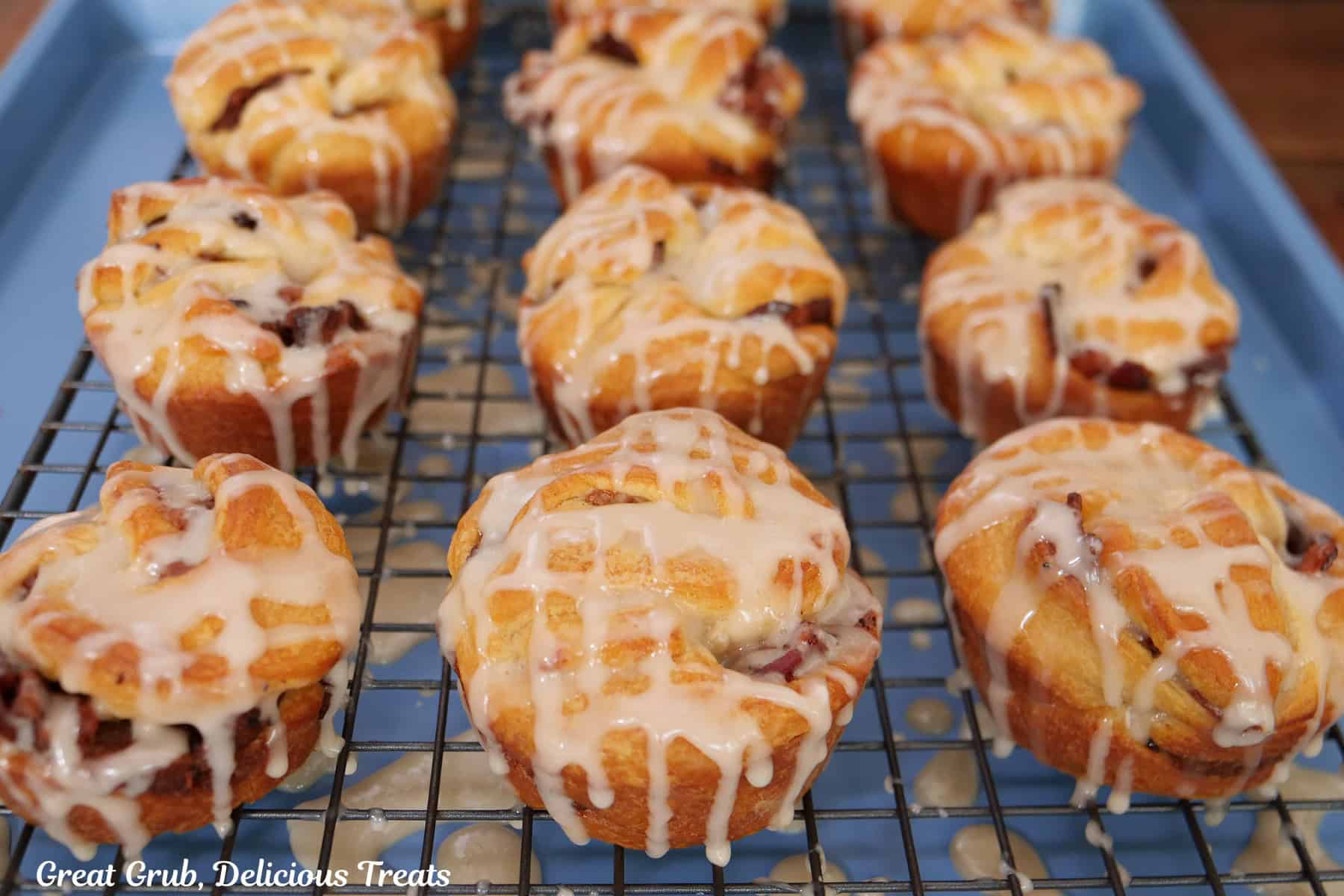 A blue baking sheet with a wire rack on top with twelve muffins that have been drizzled with maple icing.