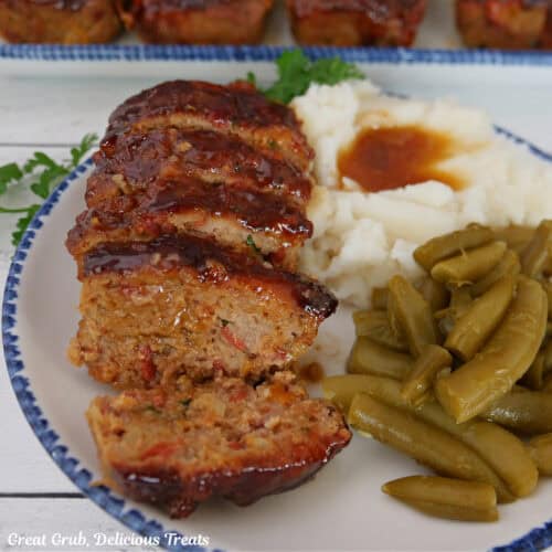 A round with plate with blue trim with a mini turkey meatloaf, mashed potatoes, and green beans on it.