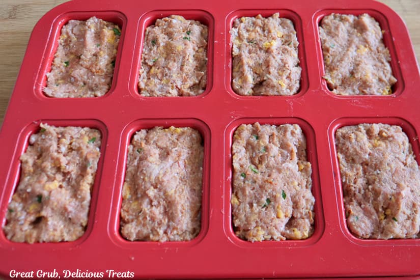 A red mini meatloaf pan with eight turkey meatloaves in it before being placed in the oven.