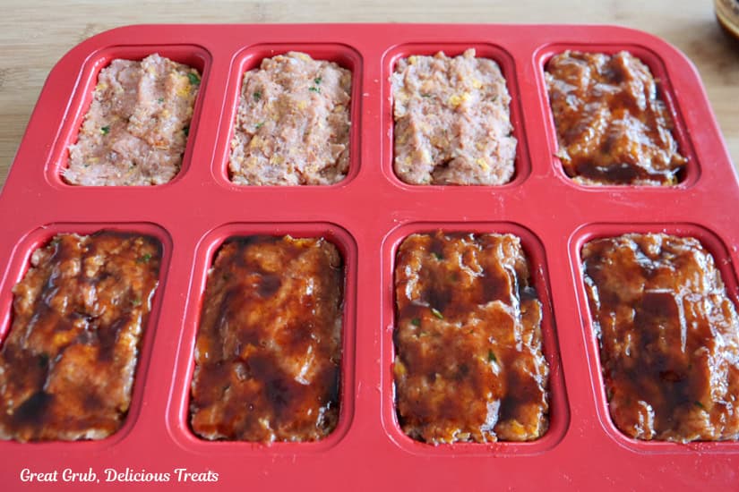 A red mini meatloaf pan with eight turkey meatloaves in it with a BBQ sauce mixture being brushed over the tops.