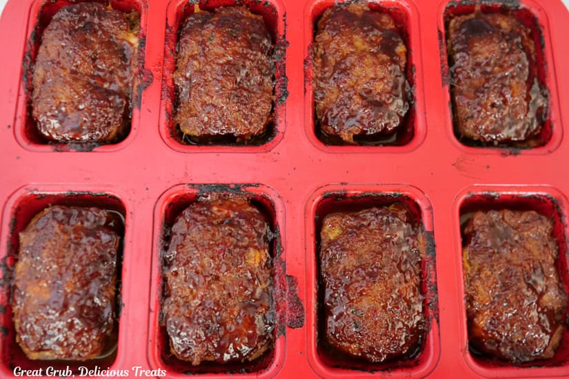 A red mini meatloaf pan with eight baked turkey meatloaves in it.