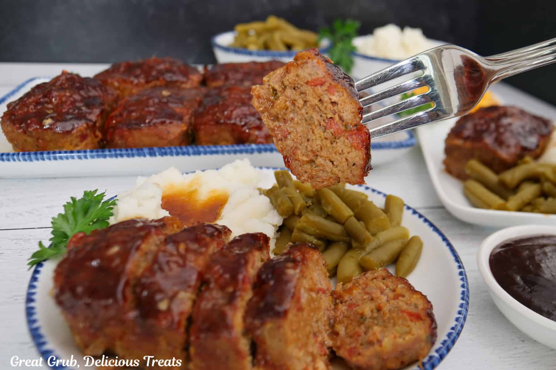 A white surface with blue trimmed white plates with mini turkey meatloaves on them with a bite of meatloaf on a fork.