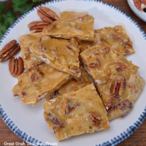 A white plate with blue trim filled with homemade pieces of pecan brittle.