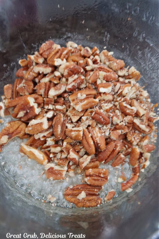 A glass bowl with boiling sugar and corn syrup with chopped pecans being added to it.