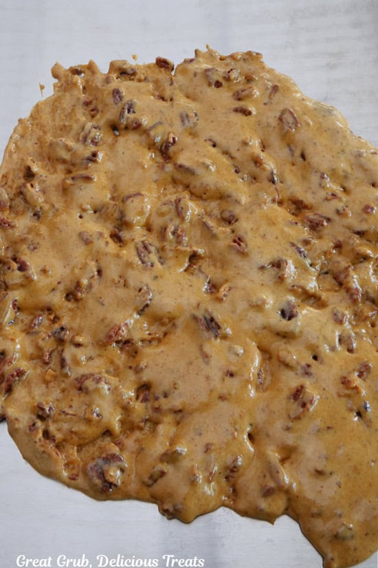 A metal baking sheet with hot pecan brittle being poured out on it and spread in an evenly layer.