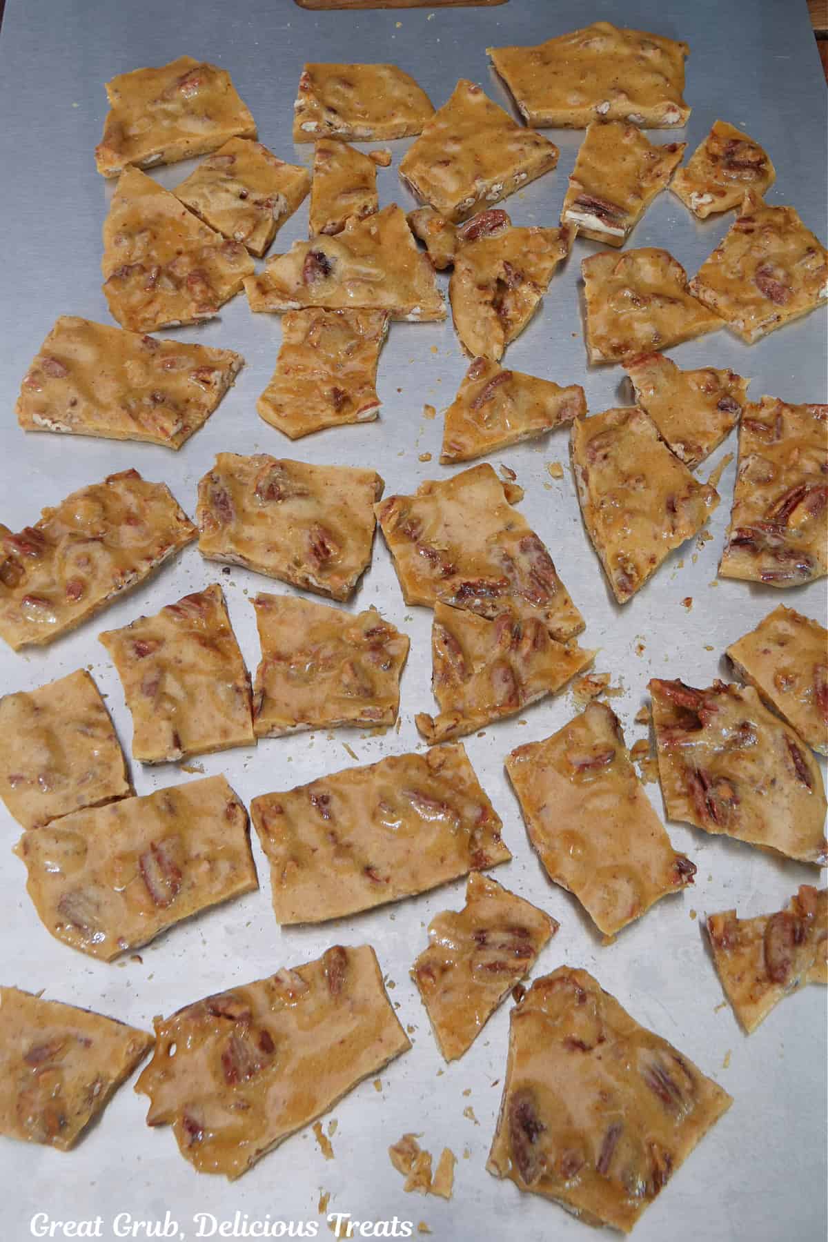 A metal baking sheet with broken pieces of pecan brittle on it.