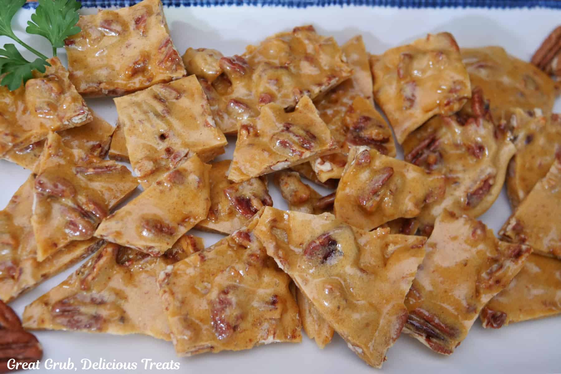 A whtie oblong plate with blue trim with pieces of homemade pecan brittle.