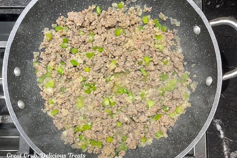 A frying pan with cooked sausage, onions, and green bell peppers in it.