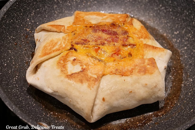A frying pan with a fried breakfast crunch wrap in it after being flipped over to fry the other side.