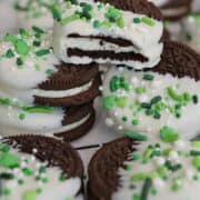 A white surface with white chocolate dipped Oreos with St. Patrick's Day sprinkles on them.