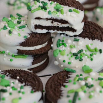 A white surface with white chocolate dipped Oreos with St. Patrick's Day sprinkles on them.