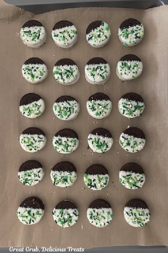 A baking sheet lined with parchment paper with 24 white chocolate dipped Oreos on it.