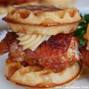 A white plate with a mini bacon wrapped chicken and waffle with honey butter on the plate.