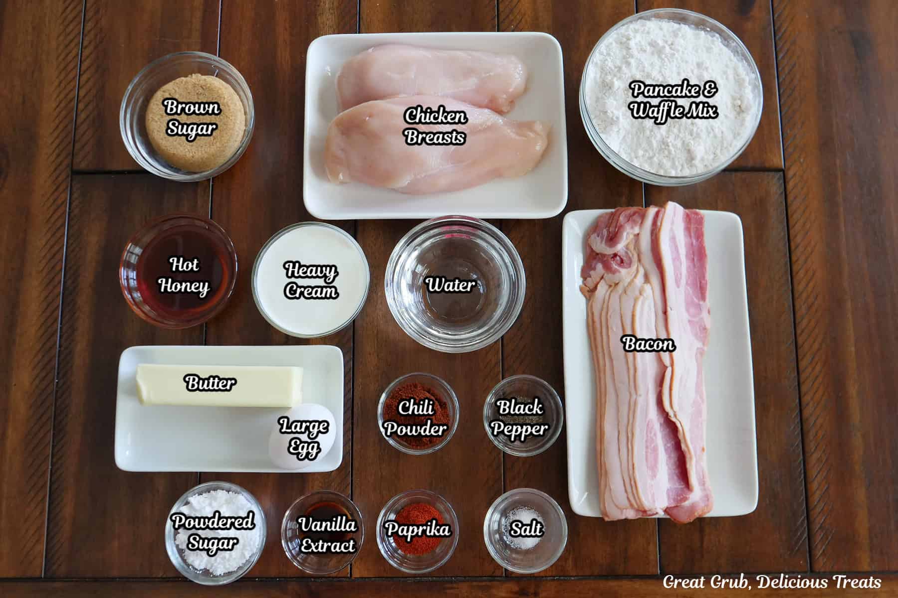 A wood surface with all the ingredients on it to make bacon wrapped chicken bites and waffles with honey butter.