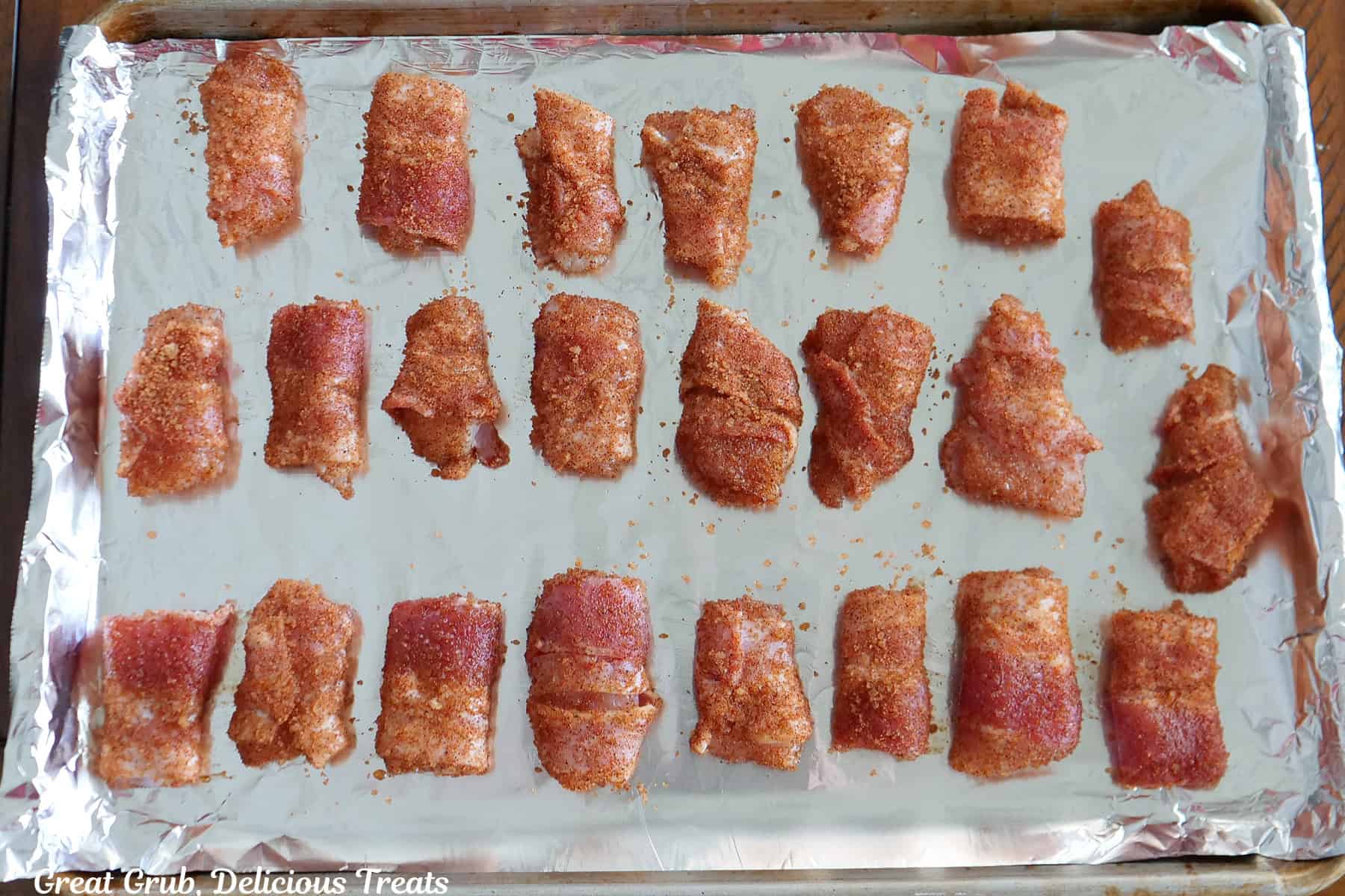A foil lined baking sheet with bacon wrapped chicken pieces that have been covered with seasonings on it, place on the baking sheet.