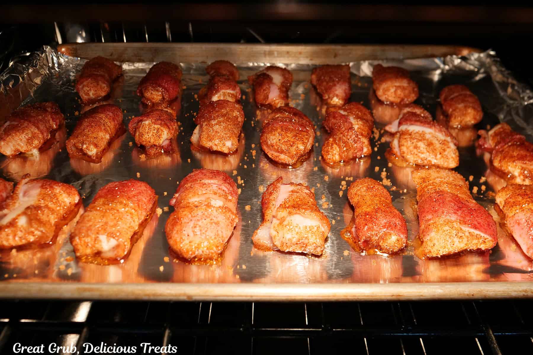 A baking sheet with bacon wrapped chicken bites on it baking in the oven