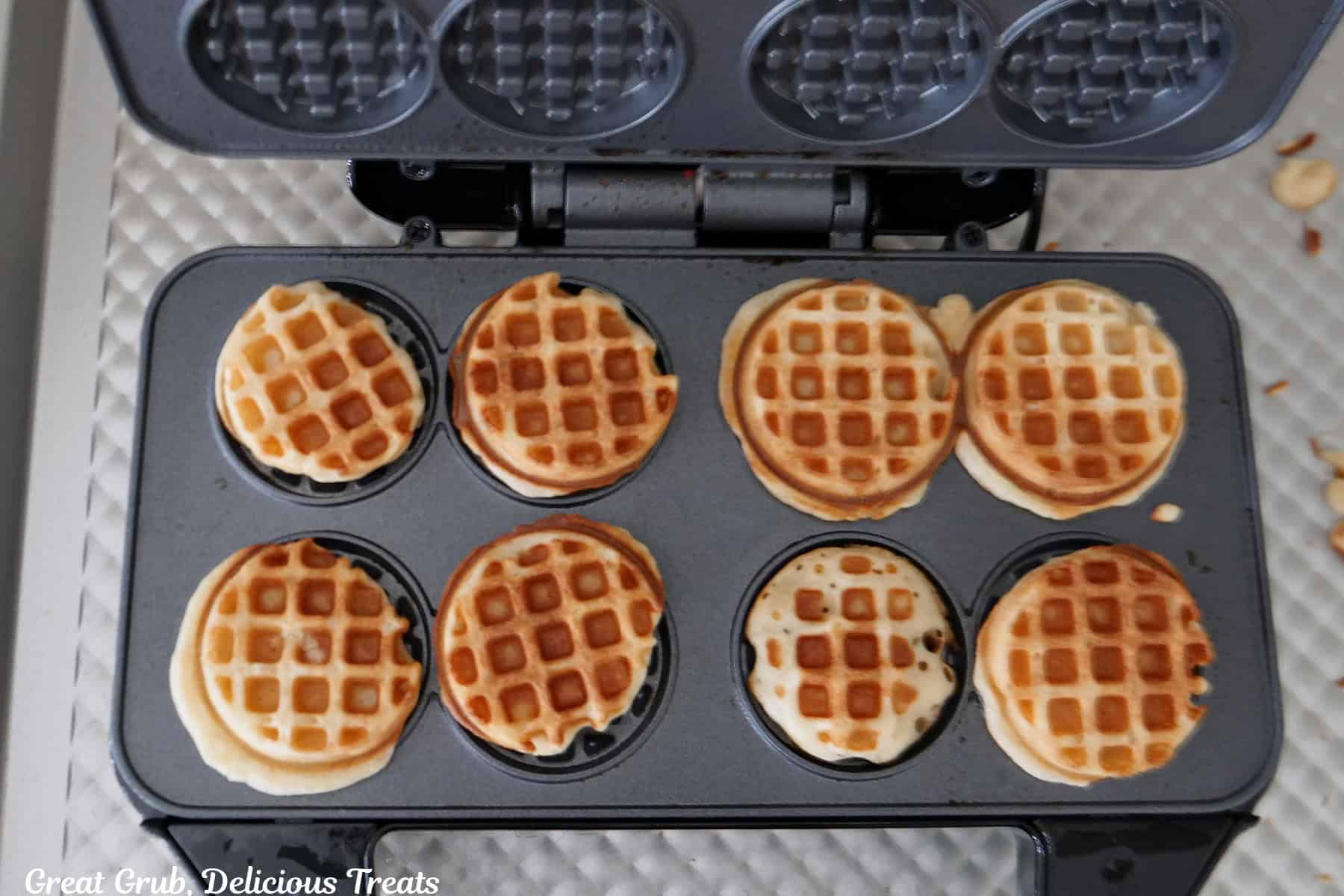 A mini waffle iron with the lid opened and cooked mini waffles in it.
