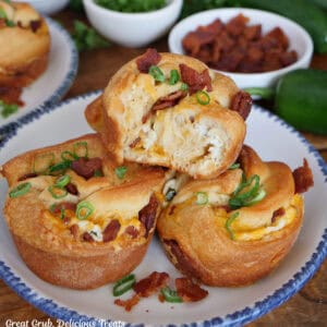 A round white plate with blue trim with four cheesy jalapeno popper muffins on it with a bite taken out of the muffin on top.