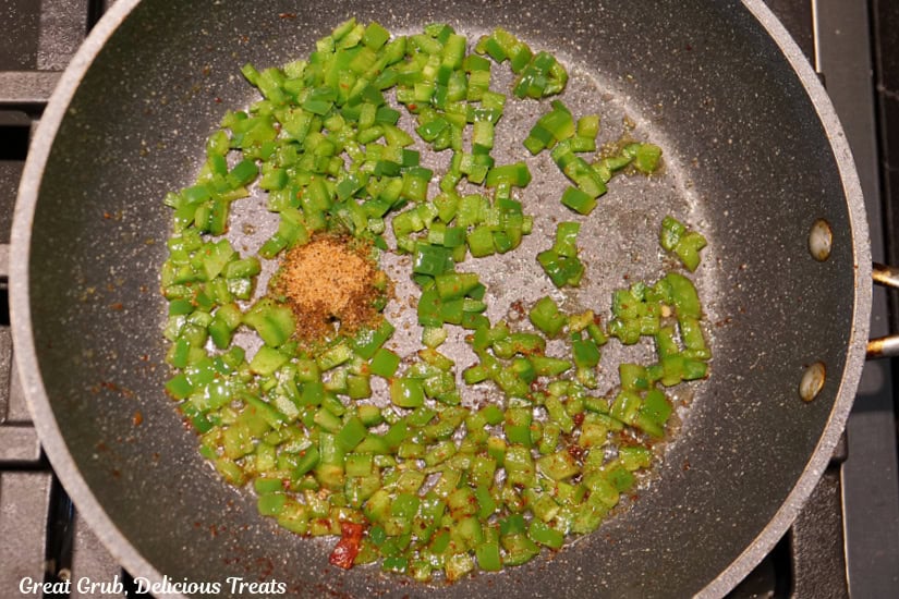 A frying pan with tender sauteed diced jalapenos and seasoning added to the pan.