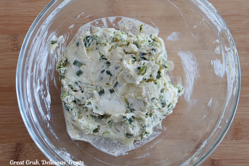 A glass bowl with cream cheese, jalapenos, and sliced green onions all mixed together.