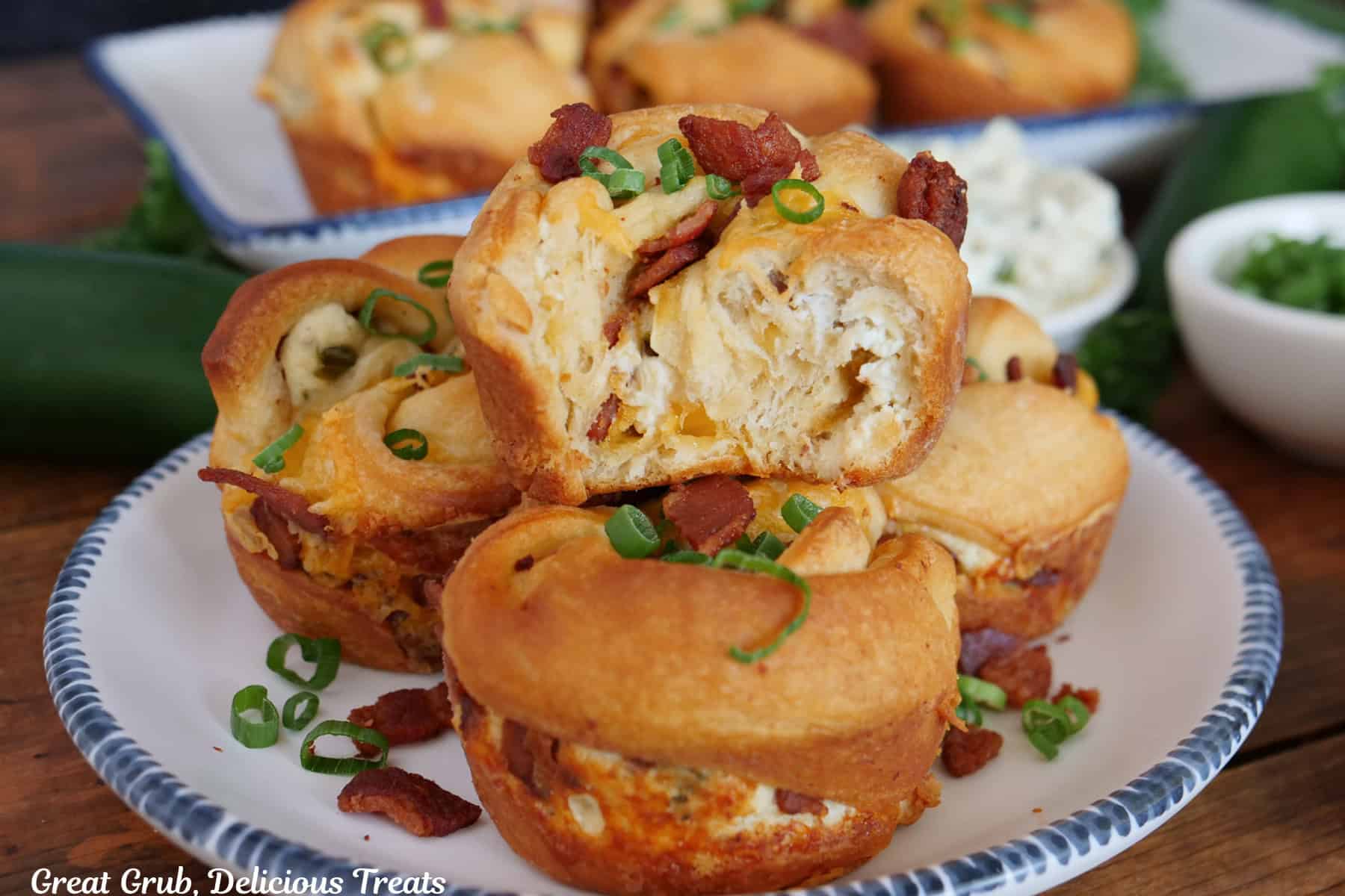 A white plate with blue trim with four cheesy jalapeno popper muffins on it with a bite taken out of the muffin placed on the top.