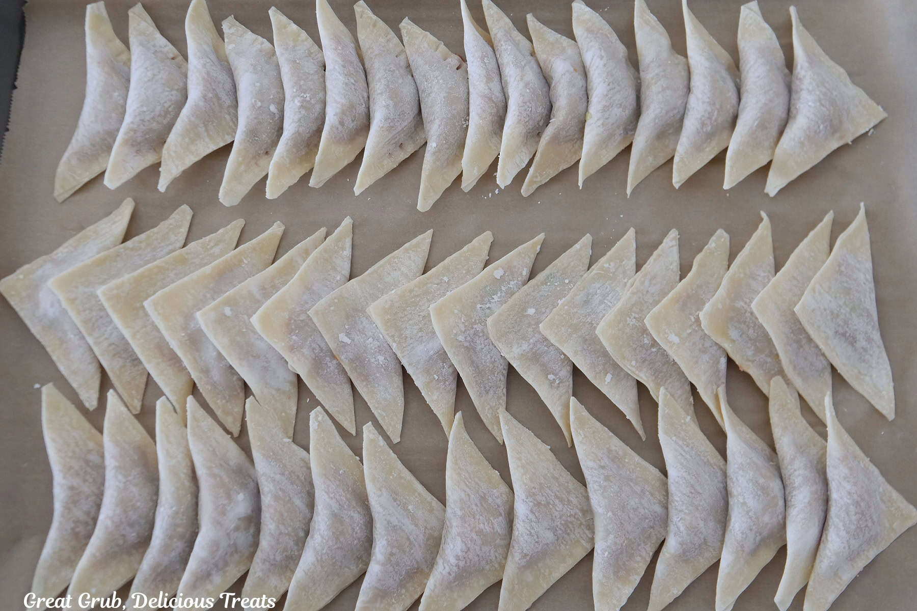 A baking sheet lined with parchment paper with approximately 37 potstickers on it before being cooked.