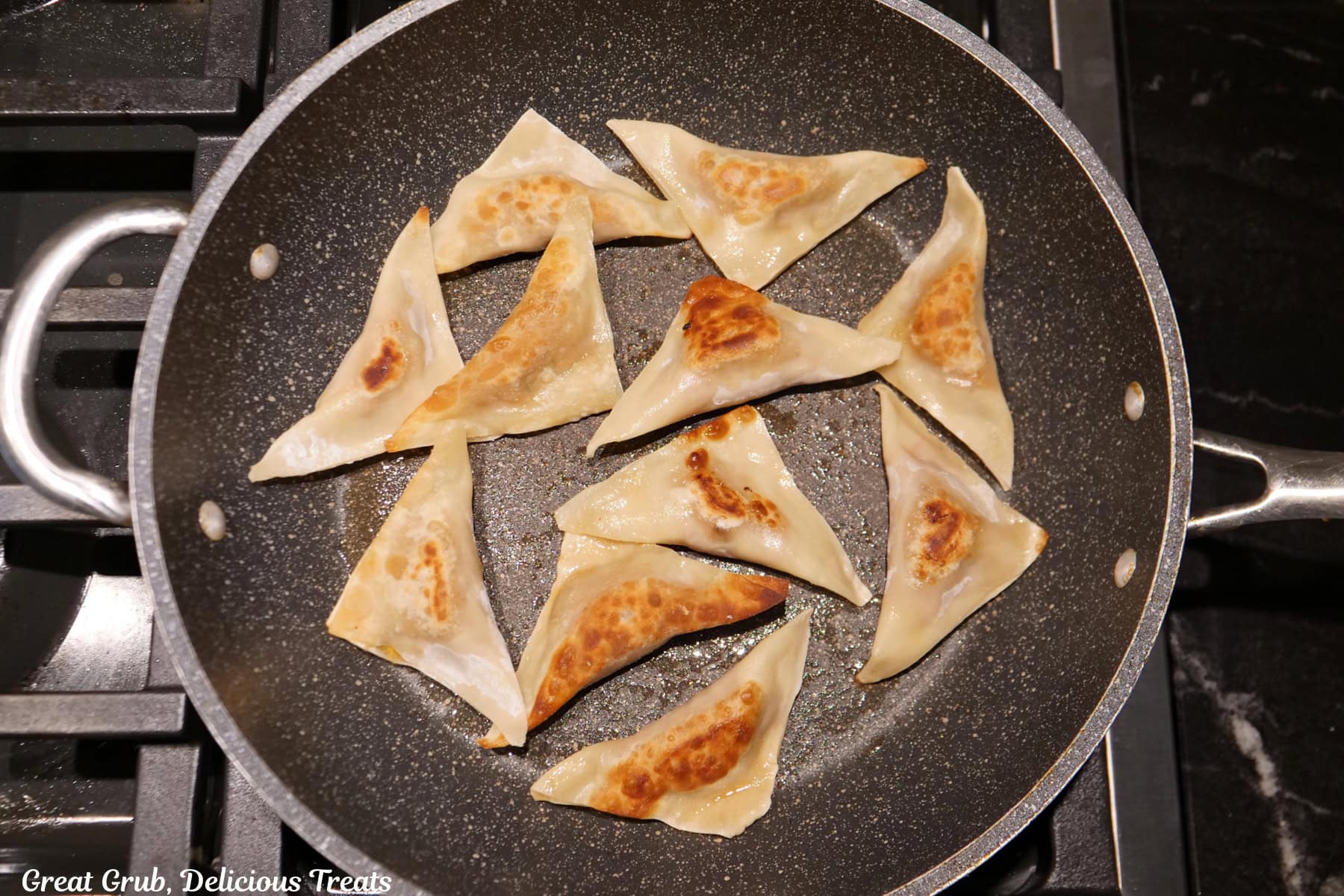 A frying pan with eleven pork potstickers in it that are browned on one side.