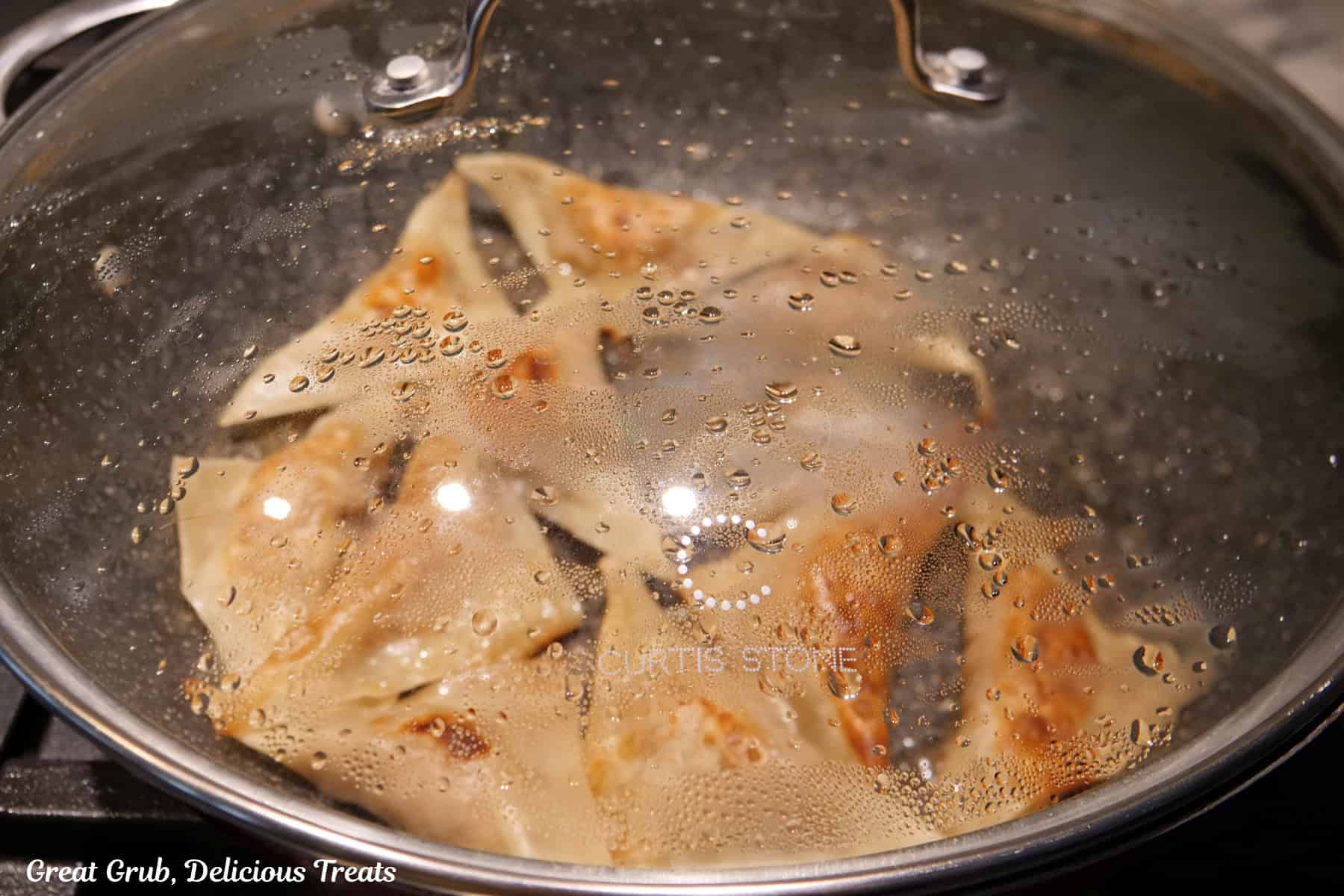 A frying pan with a lid on it steaming the potstickers.