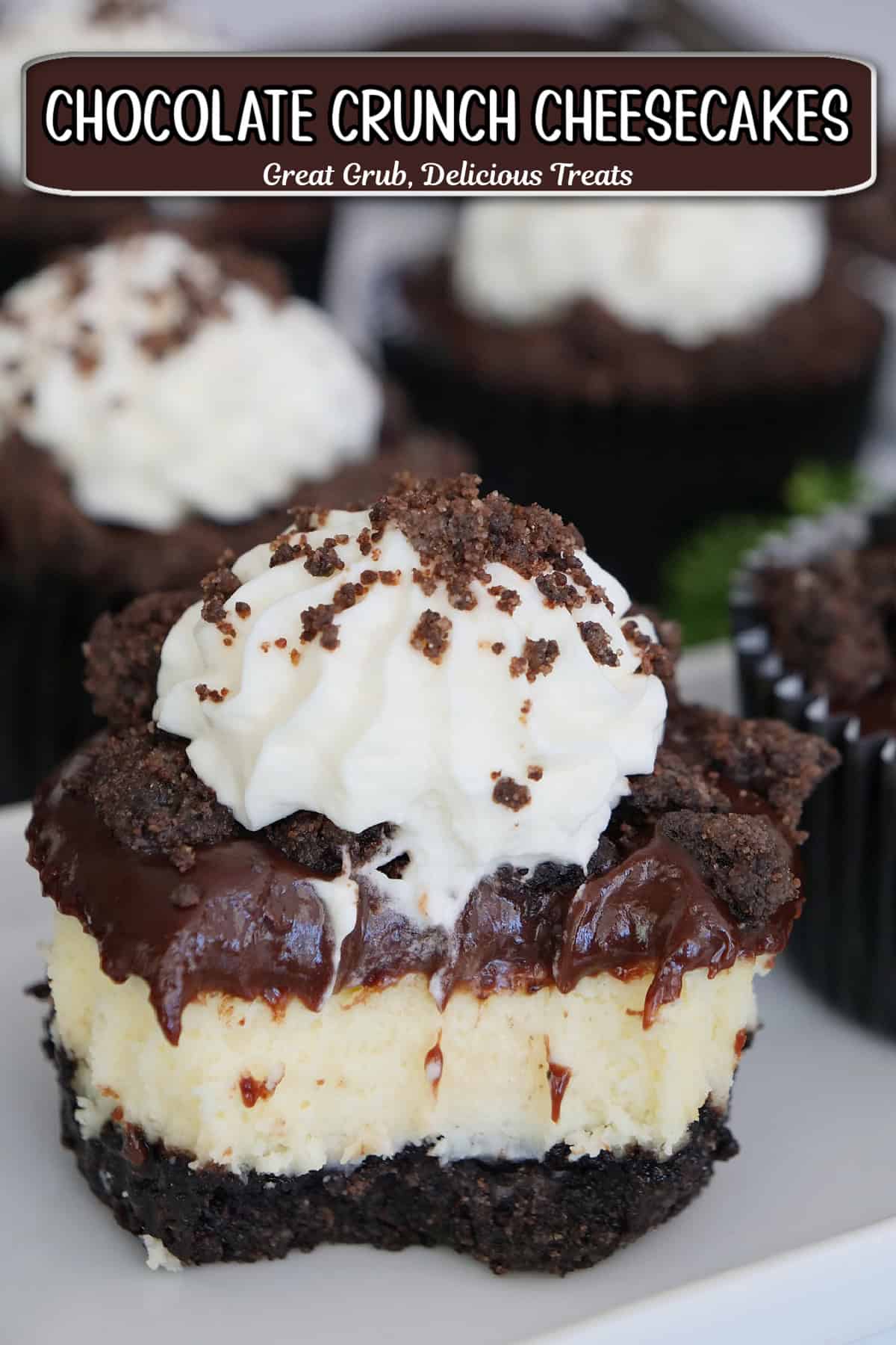 A white surface with mini chocolate crunch cheesecakes on it with a bite taken out of the one in front showing the different layers.