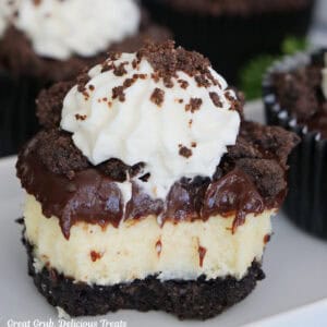 A mini chocolate crunch cheesecake on a white surface with a bite taken out of the mini cheesecake.