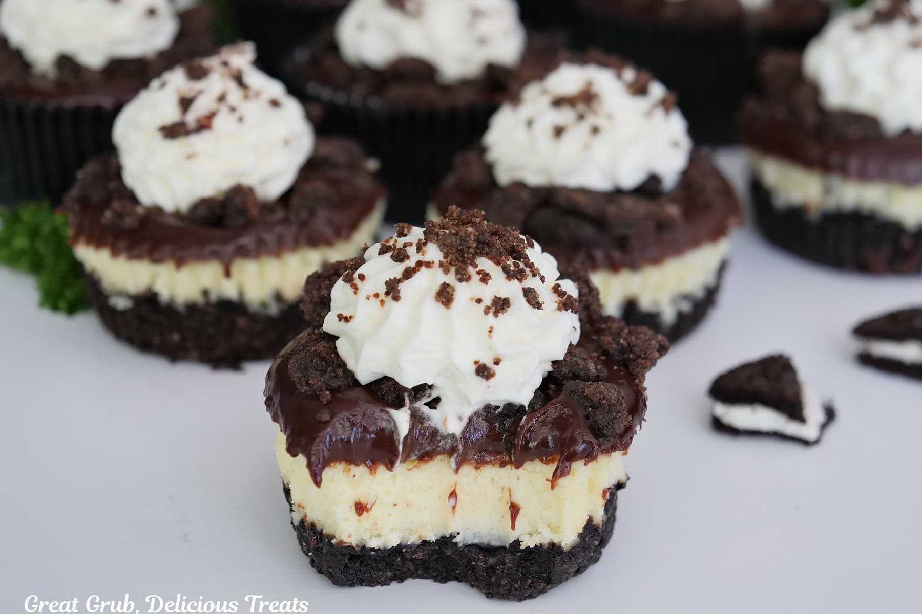 A white surface with mini chocolate crunch cheesecakes on it with a bite taken out of the cheesecake in the front.