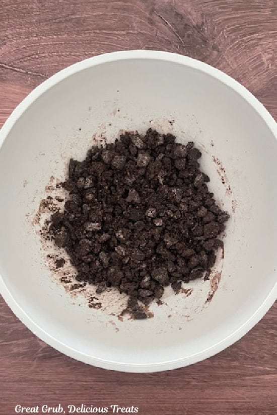 A wood surface with a white bowl with crunch Oreo cookie mixture in it.