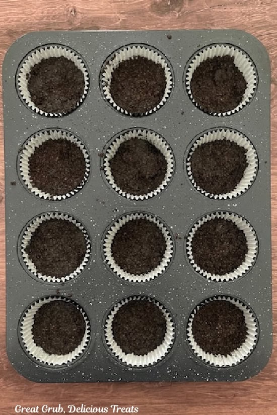 A 12-count muffin tin with paper liners in it with Oreo chocolate crunch in the bottom of each paper liner.