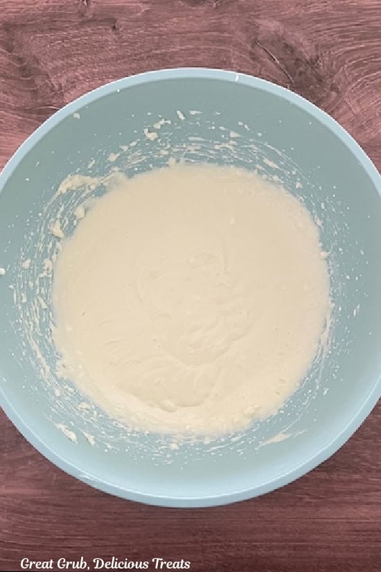 A light blue mixing bowl with the cream cheese mixture in it after being combined with all the ingredients for the mini cheesecakes.
