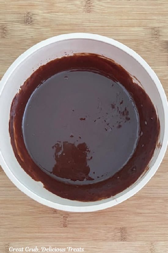 A white bowl with heavy cream and melted chocolate chips mixed together until it is smooth.