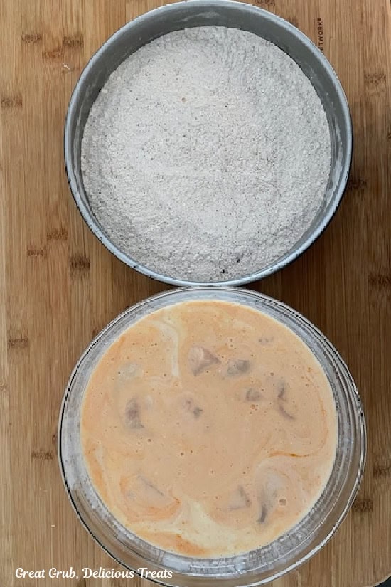 A wood surface with two bowl, one with a seasoned flour mixture, and one with the marinating chicken pieces.