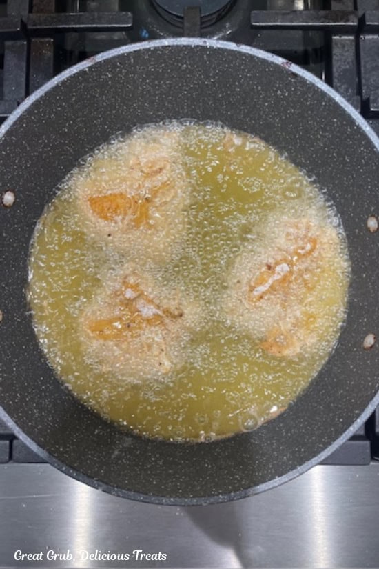 A frying pan on the stove with hot oil bubbling and fried chicken cooking in the hot oil.