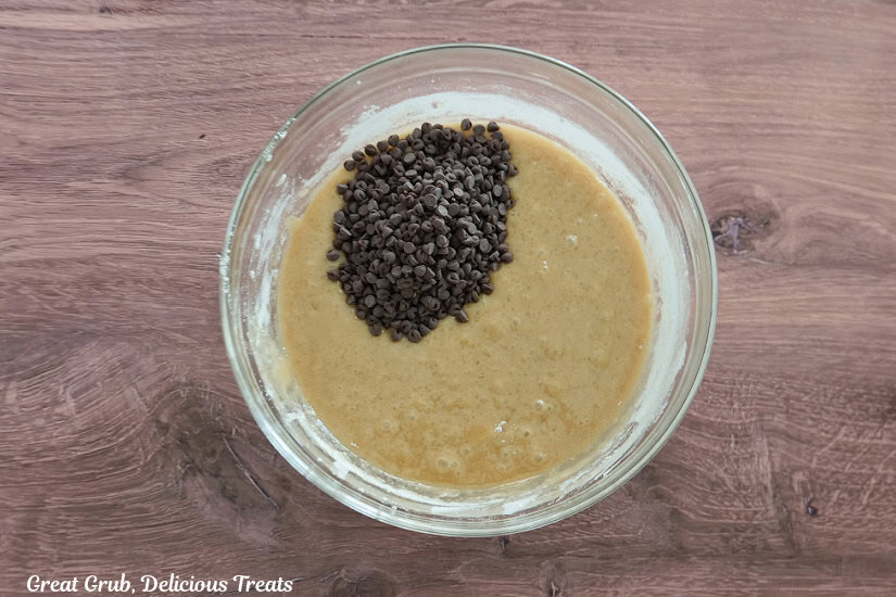 A wood surface with a glass bowl with the blondies batter mixed together and mini chocolate chips added that have not been stirred into the batter yet.