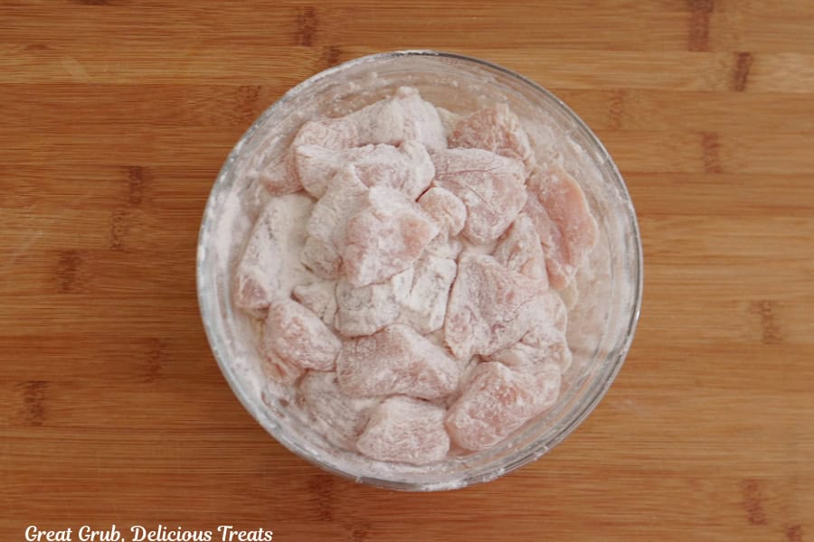 A wood surface with a glass bowl filled with chicken breasts pieces coated in tempura.