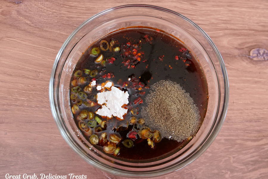 A wood surface with a glass bowl filled with all the sauce ingredients before being mixed together.